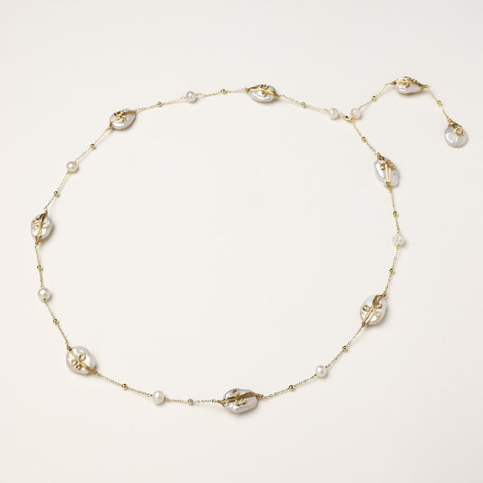 Delicate gold-plated necklace featuring translucent leaf-shaped baroque pearls and round freshwater pearls on neutral background.