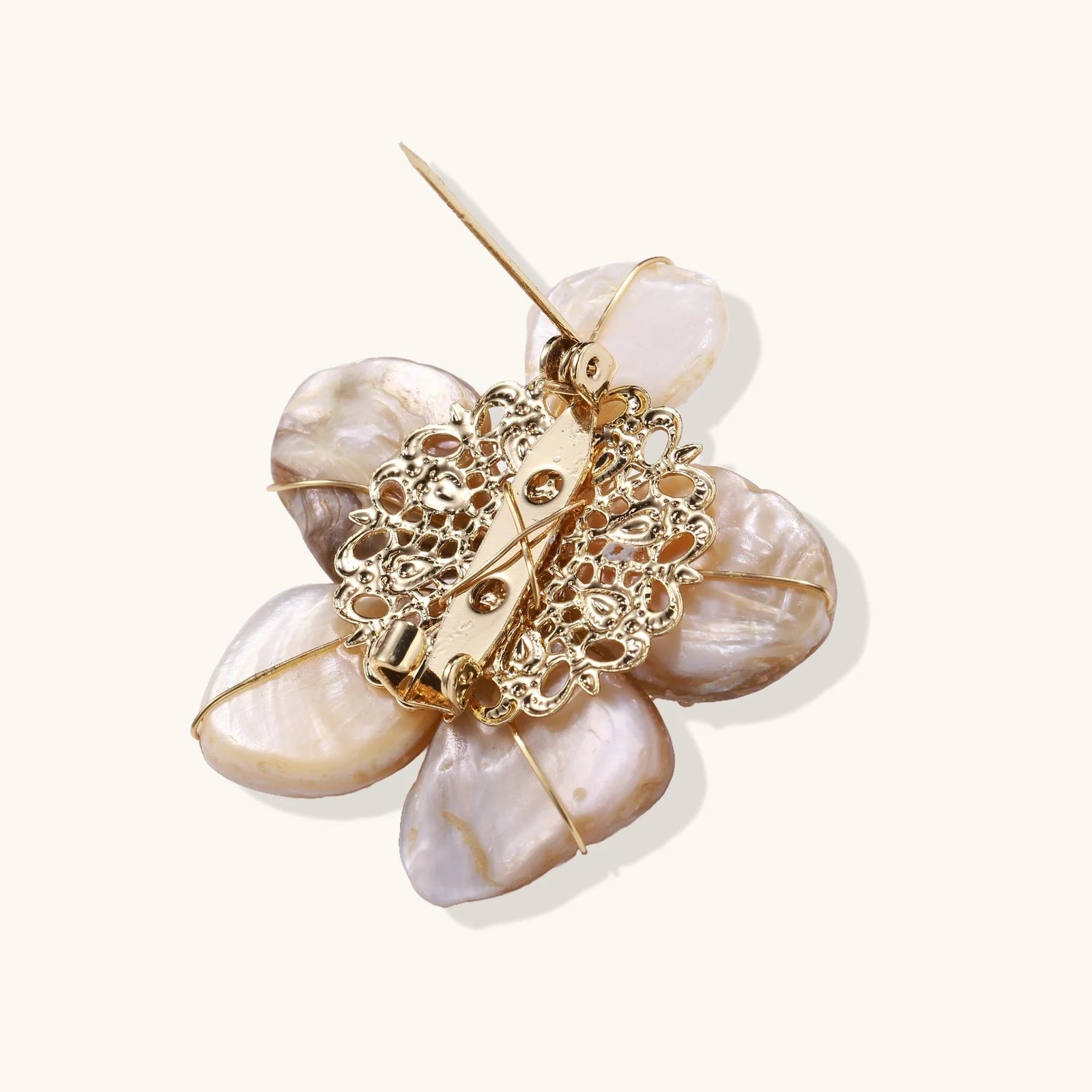 Flower-shaped brooch with iridescent shell petals, freshwater pearl center, and gold-plated radiating details.