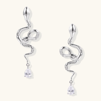 Silver snake-shaped drop earrings with crystal accents and teardrop stone dangles on cream background.