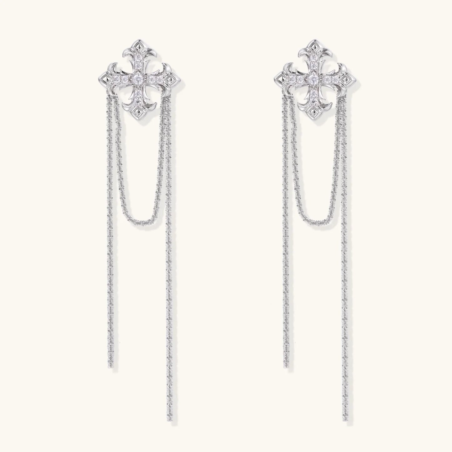 White gold plated baroque cross stud earrings with long cascading zirconia chains on cream background