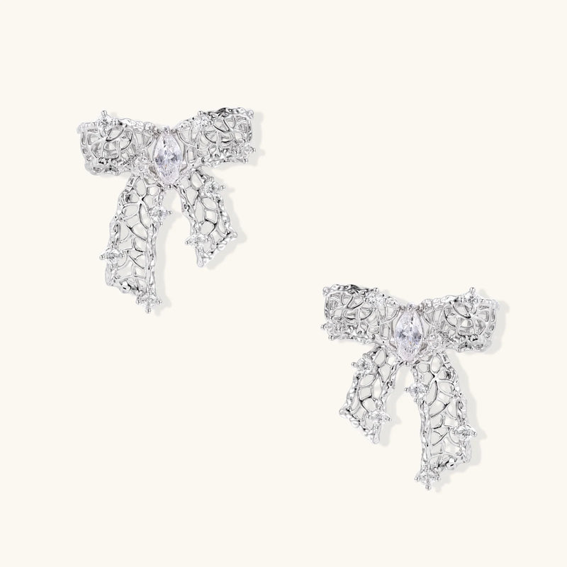 A display of the silver variant of the Ribbon Dreams Bow Earrings by Astral Signature, made from 18K Gold Plated Eco-Brass and studded with zirconia. These earrings represent luxurious Eco-Brass Earrings, an elegant Gift for Her, featuring hypoallergenic Sterling Silver (S925) posts.