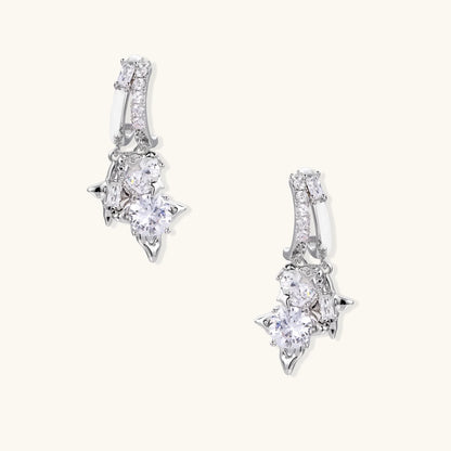 White gold-plated huggie earrings with geometric emerald-cut zirconia clusters in starburst formation on beige background