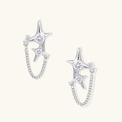 Silver star studs with crescent moon cutouts and zirconia stones connected by delicate chains on white background