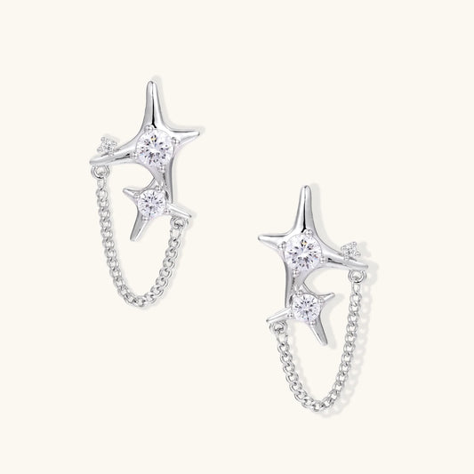 Silver star studs with crescent moon cutouts and zirconia stones connected by delicate chains on white background