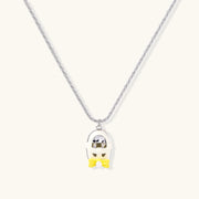 Close-up of the Cosmic Dreamer Necklace featuring a chrome egg pendant with a kawaii face and a yellow bow, designed by Astral Signature in white gold plated Eco-Brass. Perfect addition to any jewelry collection. Cosmic Dreamer Necklace, Eco-Brass Necklaces, Necklace, White Gold Plated Eco-Brass.