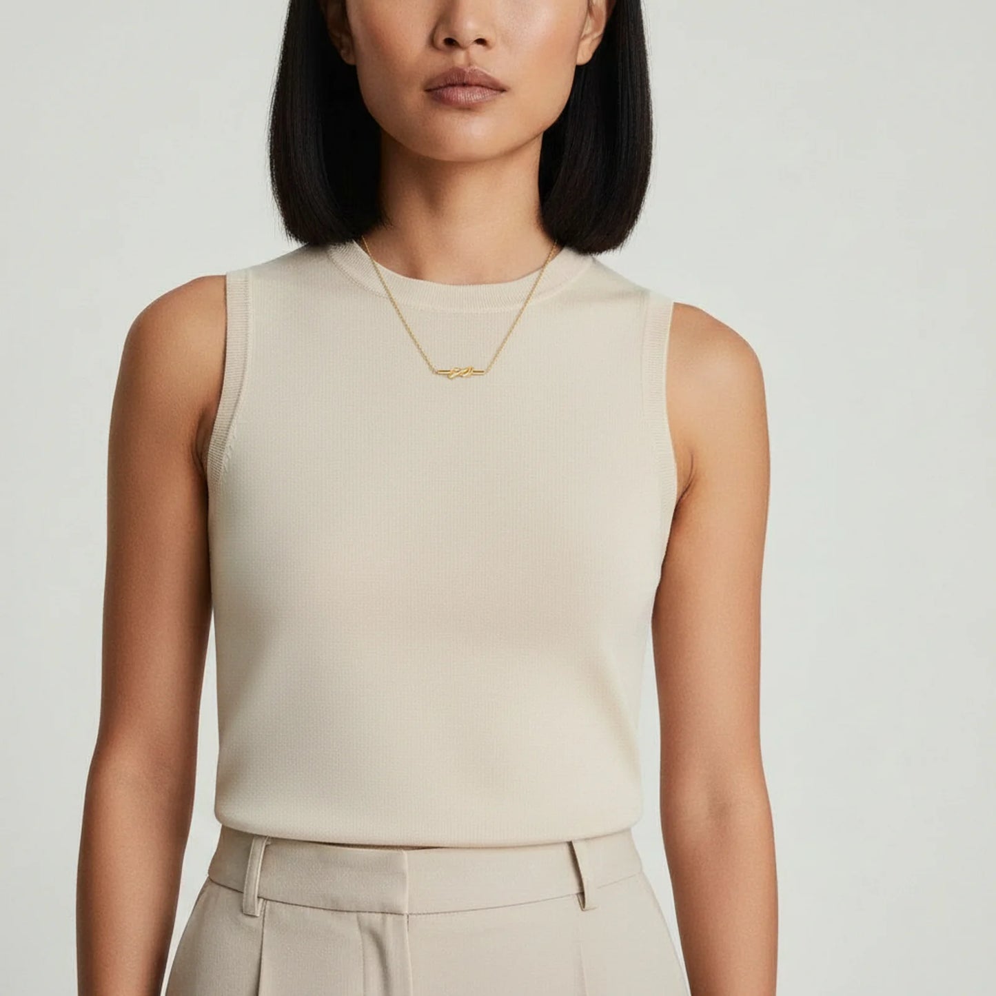 A woman in a sleeveless top proudly displaying the 18K gold-plated Unity Knot Necklace by Astral Signature™, illustrating the versatility of this stylish piece perfect for any occasion. This image represents Astral Design, making it a special Gift for Her from the Limited Edition series.