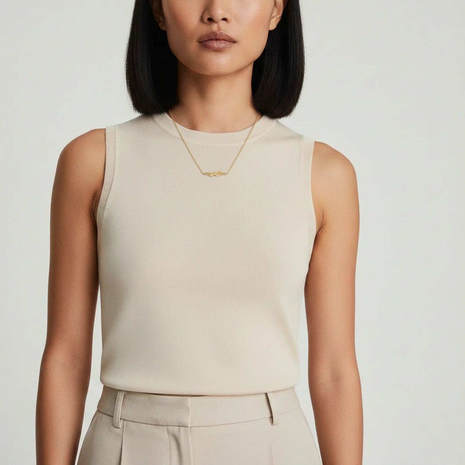 A woman in a sleeveless top proudly displaying the 18K gold-plated Unity Knot Necklace by Astral Signature™, illustrating the versatility of this stylish piece perfect for any occasion. This image represents Astral Design, making it a special Gift for Her from the Limited Edition series.