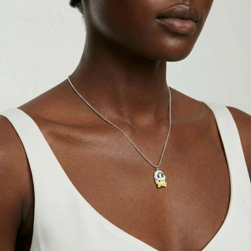 A woman modeling the Cosmic Dreamer Necklace featuring a playful design with a chrome egg pendant and yellow bow from Astral Signature, made of lightweight white gold plated Eco-Brass. Cosmic Dreamer Necklace, Eco-Brass Necklaces, Necklace, White Gold Plated Eco-Brass.
