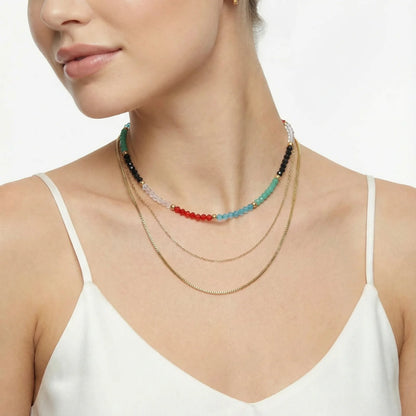 A woman elegantly wears the Rainbow Aura Layers necklace from Astral Signature, composed of 14K Gold Plated Stainless Steel and clear quartz, ideal for daily use. This distinctive piece adds a splash of color and energy, making it a perfect gift for her and part of a limited edition series.