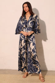 A front view of the Astral Women's Jumpsuit - Navy Orchid Lily Satin Cape by TYCHE, showcasing its sophisticated design with wide-leg and beautiful floral print. This statement piece is perfect for any special event. APPAREL, CCPRODUCTS, JUMPSUITS & ROMPERS, Navy, NEW ARRIVALS, Women's, Women's Clothing, Women's Fashion, Women's Jumpsuit, Women's Style.