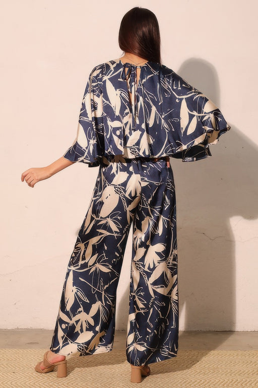Rear view of the Astral Women's Jumpsuit - Navy Orchid Lily Satin Cape by TYCHE, highlighting its stylish cape overlay and botanical print. Ideal for elevated occasions, this jumpsuit redefines women's elegance. APPAREL, CCPRODUCTS, JUMPSUITS & ROMPERS, Navy, NEW ARRIVALS, Women's, Women's Clothing, Women's Fashion, Women's Jumpsuit, Women's Style.