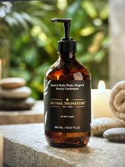 Astral Signature Hand & Body Wash, Ginger & Smoky Cardamom displayed amidst stones and candles, indicating a spa-like experience. This amber bottle contains a natural certified formula that is vegan, gluten-free, and gentle to skin, suitable for all skin types seeking hydration and cleansing.