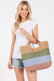 A stylish model wearing a white t-shirt and denim shorts, holding the Weekender Stripe Tote Bag by HD ACCESSORIES. This colorful beach tote bag features green, blue, and earthy hues, perfect for summer outings. Ideal for vacations and beach days, this tote is part of the new arrivals collection. The Weekender Stripe Tote Bag combines functionality and vibrant design, making it a must-have accessory.