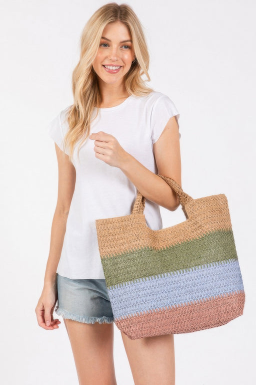 A stylish model wearing a white t-shirt and denim shorts, holding the Weekender Stripe Tote Bag by HD ACCESSORIES. This colorful beach tote bag features green, blue, and earthy hues, perfect for summer outings. Ideal for vacations and beach days, this tote is part of the new arrivals collection. The Weekender Stripe Tote Bag combines functionality and vibrant design, making it a must-have accessory.