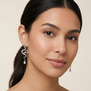 Model wearing Serpentine Crystal Drops earrings by Astral Signature, beautifully highlighting the drops made from Eco-Brass. The White Gold Plated Eco-Brass drops feature sparkling zirconia, complemented by comfortable Sterling Silver (S925) posts.
