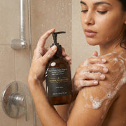 Model using Astral Signature Hand & Body Wash, Ginger & Smoky Cardamom in the shower, showcasing its luxurious lather. This vegan body wash is ideal for all skin types and is allergen label free, containing hydrating betaine and presenting a warm aroma, perfect for rejuvenating dehydrated skin.