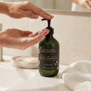 User dispensing Astral Signature Hand & Body Wash, Peppermint & Dark Cedar from a dark green bottle, emphasizing its gentle, hydrating formula. This vegan body wash, suitable for all skin types, is designed to provide allergen label free cleansing for dehydrated skin.