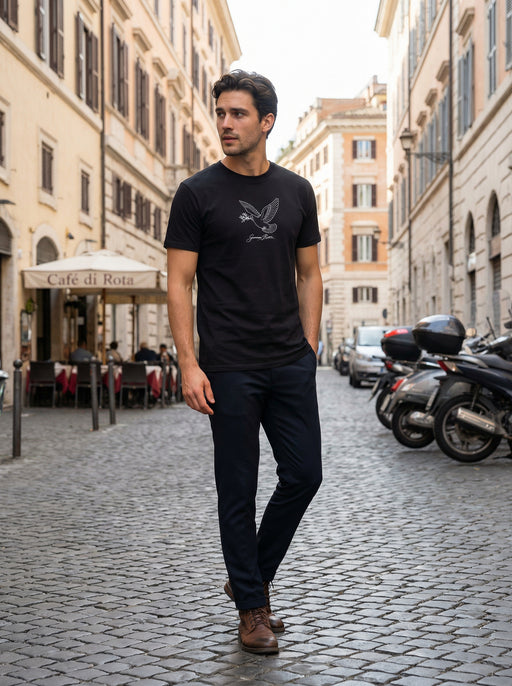 A man wearing the Giovanni Reni™ Dove Signature Tee, a Minimalist Men’s T-Shirt, walking in a cobblestone street. Ideal gift for him, this stylish men's tee combines sophistication and comfort.