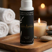 Brightening Face & Body Exfoliator with Kojic Acid by Astral Signature displayed in a serene setting. This product, packaged in white, offers mature skin types a smoothing experience while combating dark spots with hydrating ingredients like Vitamin E and Betaine.